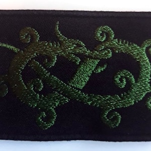Puede incluir: Parche bordado verde con un diseño estilizado de una criatura con zarcillos en espiral sobre un fondo negro.