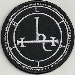 Può includere: Una toppa ricamata in bianco e nero con un sigillo con una lettera L stilizzata e una croce con un gancio all'estremità. Il sigillo è circondato da un cerchio con un motivo ripetitivo.