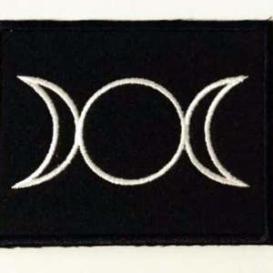 Könnte beinhalten: Ein schwarzer Stoff-Patch mit einem weißen gestickten Dreifachmond-Symbol.