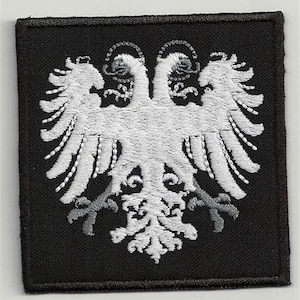 Peut inclure: Patch brodé blanc représentant un aigle bicéphale sur fond noir. L'aigle a un design détaillé avec des plumes complexes et une couronne sur la tête.
