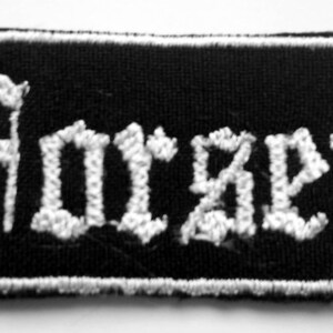 Könnte beinhalten: Schwarz-weiß gestickter Aufnäher mit dem Wort "Horzeti" in gotischer Schrift.