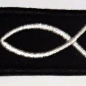 May include: A black fabric patch with a white embroidered Ichthys symbol, also known as the Jesus fish.