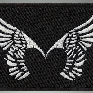 Puede incluir: Parche de tela negro con alas bordadas en blanco.