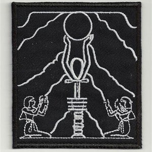 May include: Black and white embroidered patch depicting an Egyptian Ankh symbol with two figures kneeling in prayer on either side. The Ankh is raised towards a circle above, representing the sun.