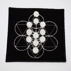 以下が含まれることがあります： 白い幾何学模様が刺繍された黒いパッチ。模様は円、三角形、線で構成されており、複雑で精巧なパターンを形成しています。