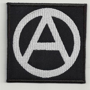 Op de afbeelding: Zwarte stoffen patch met een wit geborduurd anarchiesymbool, een cirkel met een 'A' erin.
