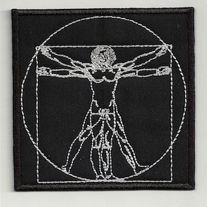 Op de afbeelding: Een zwarte geborduurde patch met een witte omtrek van een menselijke figuur in een cirkel en een vierkant. De figuur staat in de Vitruviusman-pose, met uitgestrekte armen en licht gespreide benen.