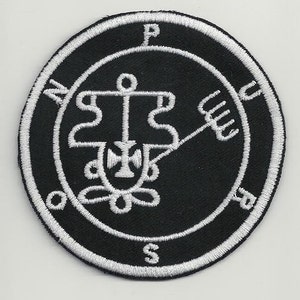 May include: A black and white embroidered patch featuring a sigil, a circle with a symbol inside, and the letters N, S, E, W, and P around the circle.