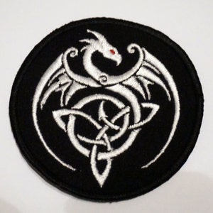 Op de afbeelding: Zwarte ovale patch met een witte geborduurde draak met rode ogen, omringd door een Keltisch knoopontwerp.