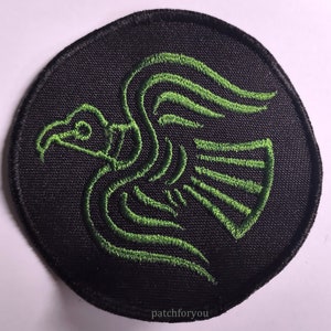 Puede incluir: Un parche bordado verde de un pájaro estilizado sobre un fondo circular negro. El parche tiene el texto "patchforyou" en la parte inferior.