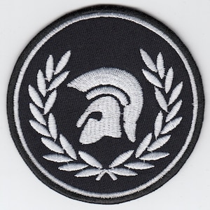 Op de afbeelding: Zwart-witte geborduurde patch met een witte Spartaanse helm met een lauwerkrans eromheen.