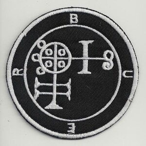 Pode incluir: Um remendo bordado preto e branco com um selo, um símbolo de um demônio, cercado por um círculo com letras. O selo é uma figura estilizada com uma cruz e um círculo que contém círculos menores.