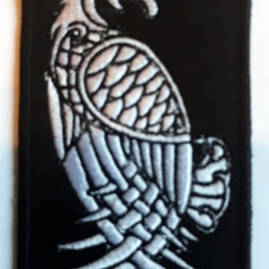 Op de afbeelding: Een zwarte geborduurde patch met een witte gestileerde adelaar met een rood oog. De adelaar kijkt naar rechts en heeft zijn vleugels uitgespreid.