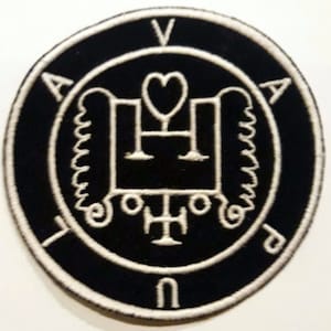 Pode incluir: Um remendo bordado preto e branco com um design circular. O centro do círculo apresenta um símbolo branco com um coração e uma cruz. O círculo é rodeado por uma borda branca com as letras "V", "A", "U" e "N" ao redor da borda.