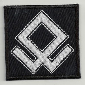 Pode incluir: Patch preto com um símbolo branco bordado. O símbolo é uma forma de diamante duplo estilizada.