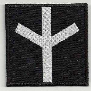 Op de afbeelding: Wit geborduurd symbool op een zwarte stoffen patch. Het symbool is een gestileerd kruis met een verticale lijn en twee diagonale lijnen die zich uitstrekken vanaf de bovenkant van de verticale lijn.