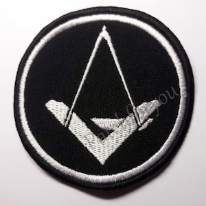 Könnte beinhalten: Ein gestickter schwarzer und weißer Aufnäher mit einer weißen Dreiecksform in einem Kreis. Das Dreieck ist weiß umrandet und hat eine weiße Linie in der Mitte.