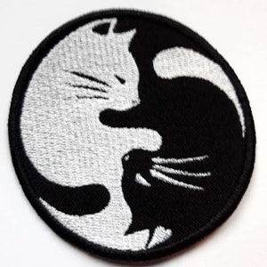 Op de afbeelding: Zwart-witte geborduurde patch van twee katten in een yin yang ontwerp.