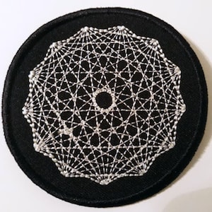Op de afbeelding: Een ronde, zwarte patch met een wit, geometrisch ontwerp. Het ontwerp heeft een centrale cirkel omgeven door een complex web van elkaar kruisende lijnen, waardoor een symmetrisch patroon ontstaat. De patch is waarschijnlijk voor kleding of accessoires.