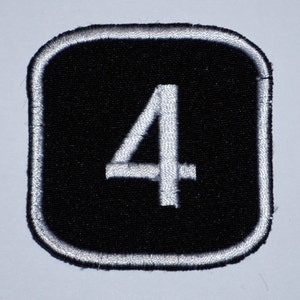 Pode incluir: Um remendo bordado preto e branco com o número 4 em branco sobre um fundo preto. O remendo tem uma borda branca.