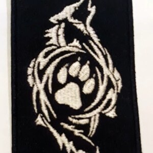May include: White embroidered patch on a black background featuring a wolf howling with a paw print inside a circle.