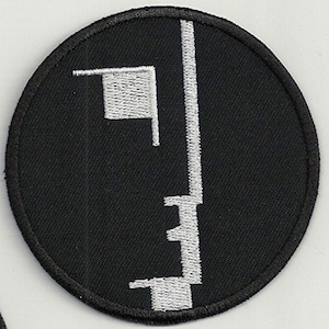 Pode incluir: Um remendo bordado preto e branco com um rosto estilizado com contorno branco. O remendo é circular e tem um fundo preto.