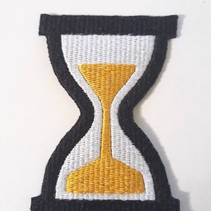 May include: Black and white embroidered patch with a yellow hourglass design.