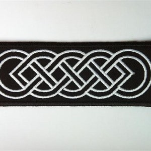 Könnte beinhalten: Ein schwarzer Stoff-Patch mit einem weißen gestickten keltischen Knotendesign. Der Knoten ist ein durchgehendes Muster aus ineinandergreifenden Schleifen.