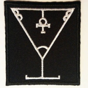 Può includere: Toppa ricamata bianca su sfondo nero. La toppa presenta un'immagine stilizzata di un bicchiere da martini con un simbolo ankh nella parte superiore.