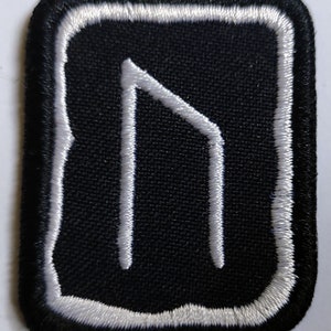 Op de afbeelding: Wit geborduurd runesymbool op een zwarte stoffen patch met een witte rand.