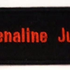 Könnte beinhalten: Schwarzer Stoff-Patch mit rotem gesticktem Text, der "...Adrenaline Junkie..." lautet.