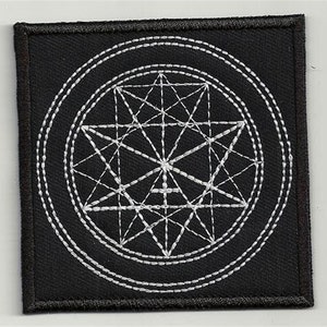 May include: Black fabric patch with a white embroidered geometric design. The design features a circle with a star inside, surrounded by a series of concentric circles.
