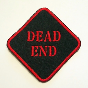 Può includere: Una toppa nera a forma di diamante con un bordo rosso. Il testo "DEAD END" è ricamato in rosso sulla toppa.