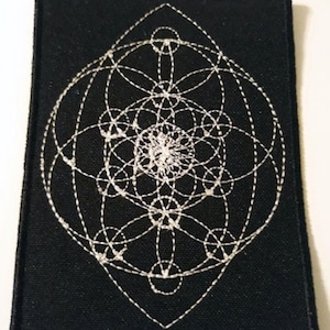 May include: A black fabric patch with a white embroidered geometric design. The design is a series of overlapping circles and lines that create a complex pattern.