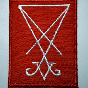 May include: A red embroidered patch featuring a white inverted pentagram symbol. The symbol is a five-pointed star with the points facing inwards.