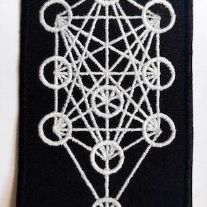 Pode incluir: Patch de tecido preto com um design geométrico bordado em branco. O design é um padrão complexo de círculos e linhas, que se assemelha a um símbolo de geometria sagrada.