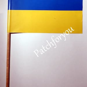 Può includere: Una piccola bandiera blu e gialla su un bastone di legno. La bandiera è la bandiera nazionale dell'Ucraina.