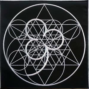 Può includere: Un cerotto in tessuto nero con un disegno geometrico ricamato bianco. Il disegno presenta cerchi, triangoli e linee sovrapposti.