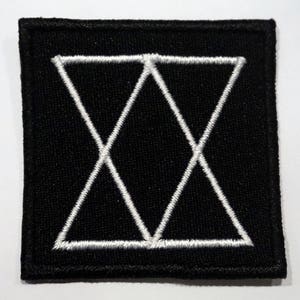 Op de afbeelding: Zwarte geborduurde patch met een wit geometrisch ontwerp van overlappende driehoeken.