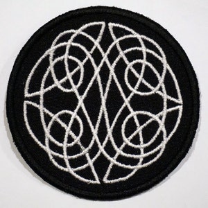 Könnte beinhalten: Ein gestickter Patch in Schwarz und Weiß mit einem kreisförmigen Design aus komplizierten weißen Linien auf schwarzem Hintergrund.
