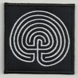 Puede incluir: Un parche bordado en blanco y negro con un diseño de laberinto circular. El laberinto tiene siete círculos concéntricos con un camino central que conduce al centro.