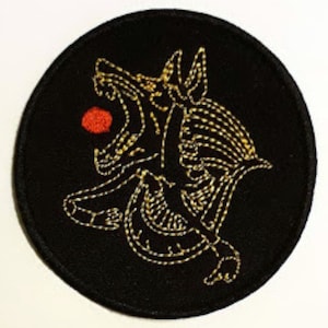 May include: A black embroidered patch with a gold outline of a snarling wolf with a red circle in its mouth.