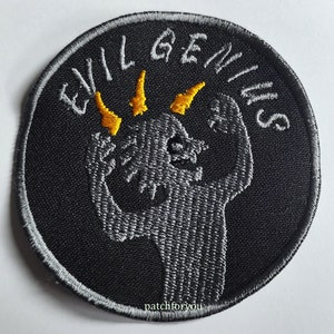 Op de afbeelding: Zwarte geborduurde patch met de tekst "Evil Genius" in witte borduurwerk. Een grijs geborduurde figuur met gele hoorns bevindt zich in het midden van de patch.