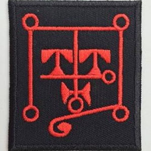 Peut inclure: Patch brodé rouge avec un motif géométrique sur fond noir. Le motif présente un carré avec des cercles à chaque coin, une ligne verticale avec deux lignes horizontales et une ligne courbe avec un cercle à l'extrémité.