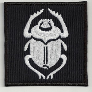 Può includere: Toppa di stoffa nera con uno scarabeo bianco ricamato.