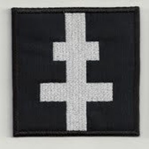Op de afbeelding: Zwart vierkantige patch met een wit dubbelbalkkruisontwerp. Het kruis is gecentreerd op de patch en heeft een getextureerde uitstraling. De patch heeft een zwarte rand en is waarschijnlijk gemaakt van stof.