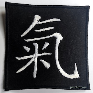 Può includere: Toppa di tessuto nero con un carattere kanji ricamato in bianco. Il carattere è "風" che significa "vento".
