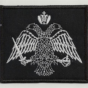 Peut inclure: Patch brodé blanc sur fond noir représentant un aigle à deux têtes surmonté d'une couronne et tenant des épées dans ses serres.