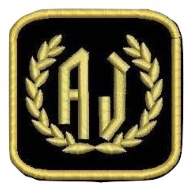 Pu&ograve; includere: Una toppa quadrata nera con una corona di alloro ricamata in oro che circonda le lettere "AJ" in un carattere stilizzato.
