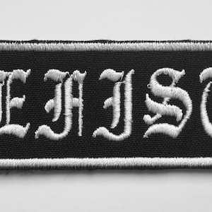 Pode incluir: Etiqueta branca bordada em fundo preto com o texto "MEFISTO" em fonte gótica.